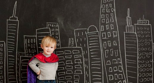 Cute toddler boy (2-3) standing against blackboard with city skyline drawn on it